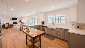 A modern kitchen with wooden flooring, white cabinets, and a dining area with a table and chairs. - Beautiful 5bedroom waterfront cottage with Hot Tub (South River)