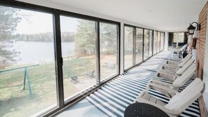 A sunlit room with large windows overlooking a lake, featuring striped flooring and a row of sun loungers. - Beautiful 5bedroom waterfront cottage with Hot Tub (South River)