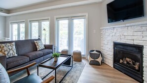 A living room with a sofa, coffee table, ottoman, fireplace, and a TV mounted on the wall.