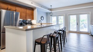 A modern kitchen with a central island, bar stools, stainless steel appliances, and a view through large windows.