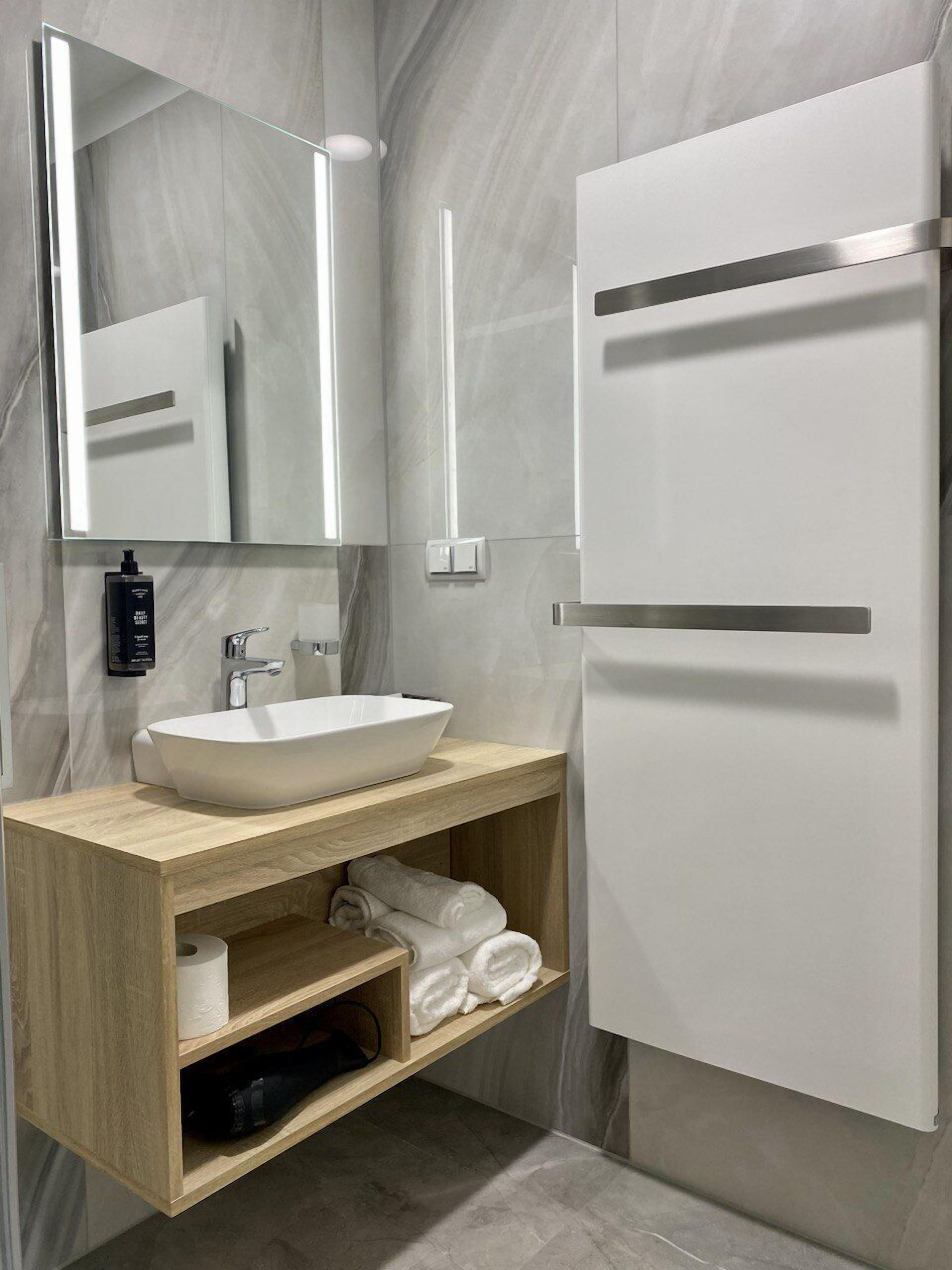 A modern bathroom with a white sink, wooden vanity, and a mirror.