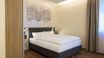 A modern bedroom with a large bed, a headboard with built-in lighting, and a wall-mounted artwork depicting buildings.