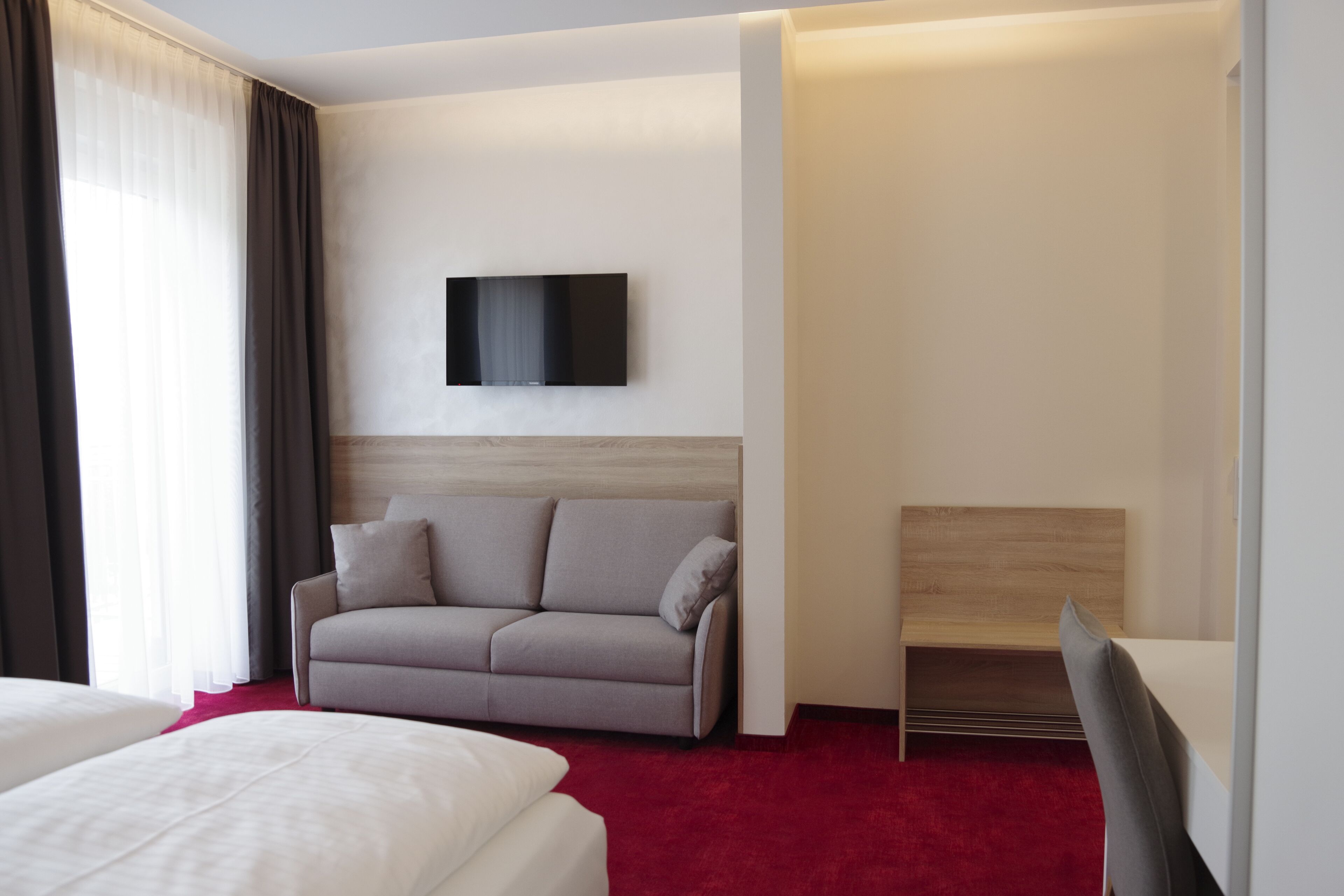 Una habitación de hotel moderna con sofá cama, televisor de pantalla plana en la pared y cama separada.