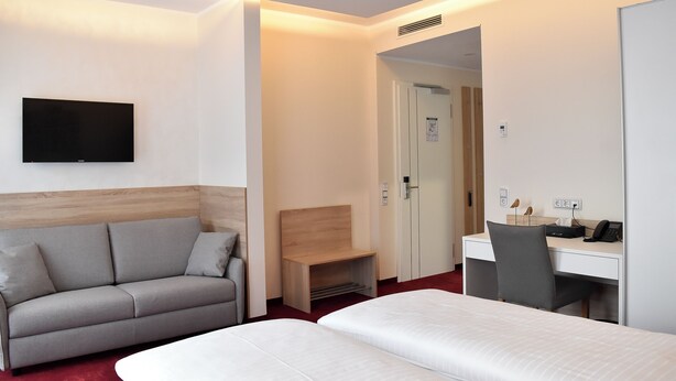 Een hotelkamer met een bed, een bureau, een stoel, een bank en een televisie.