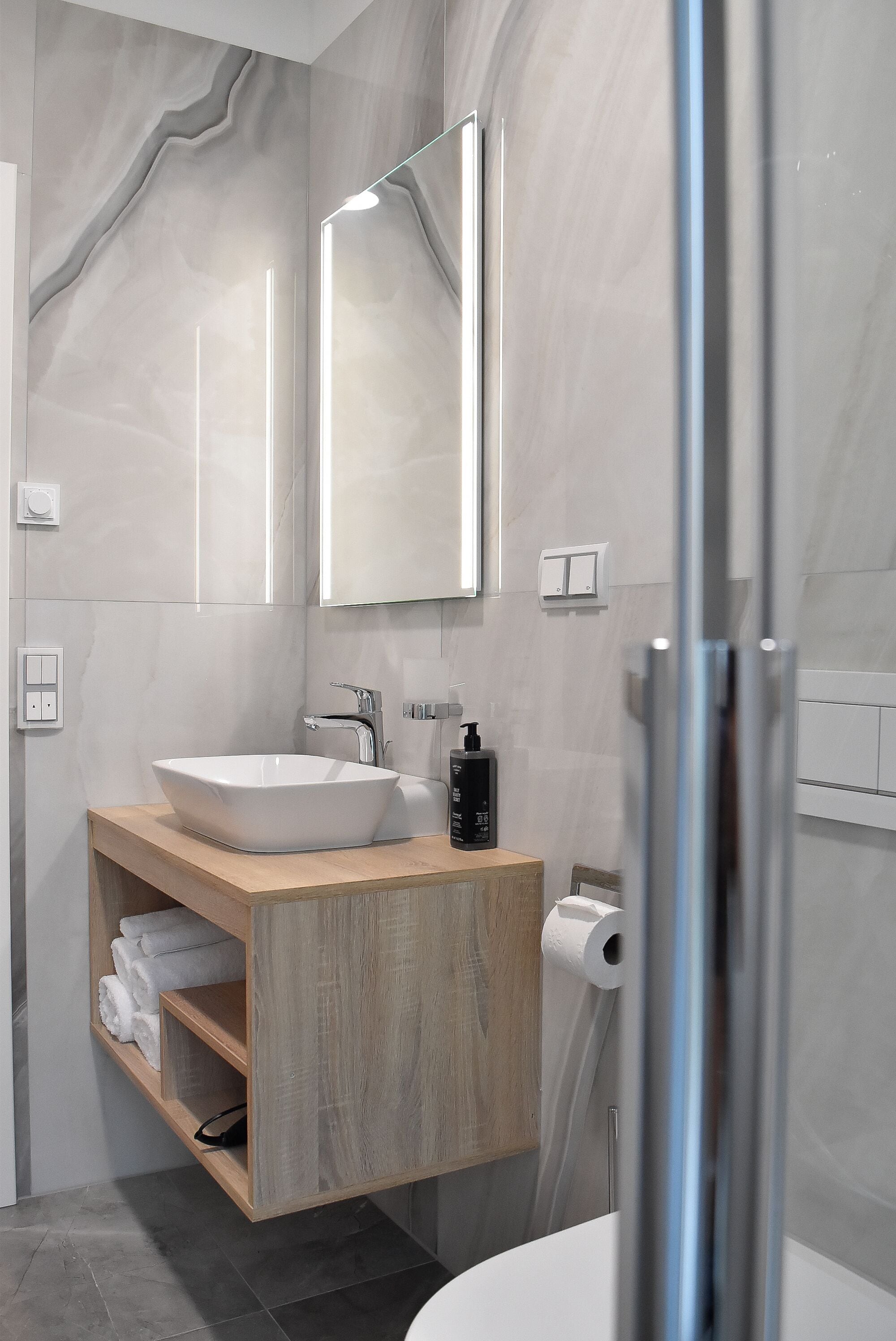 Une salle de bain moderne avec un grand miroir, un lavabo sur colonne, un meuble-lavabo en bois et un espace douche.