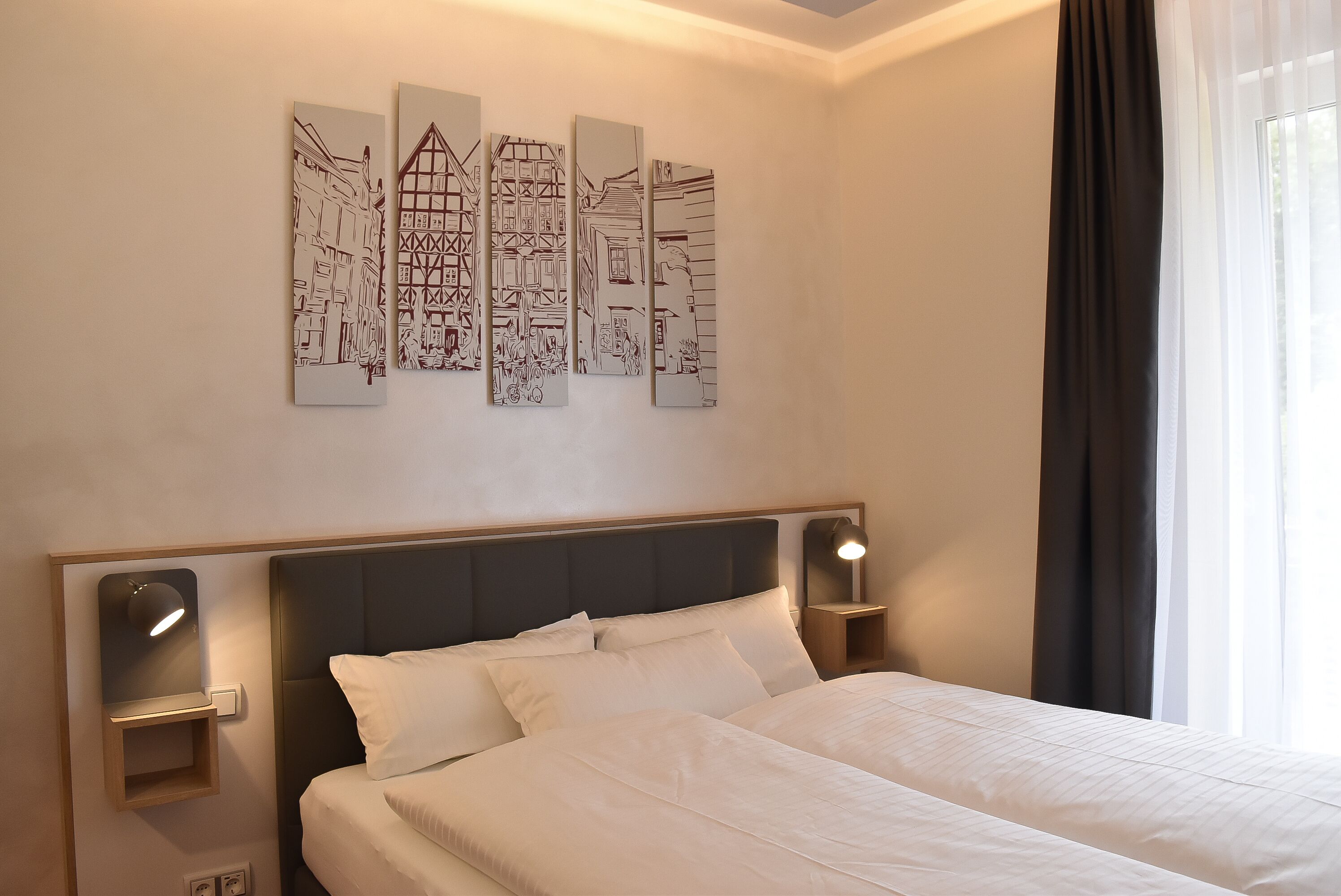 A hotel room with a bed, bedside tables, wall art, and a window with curtains.