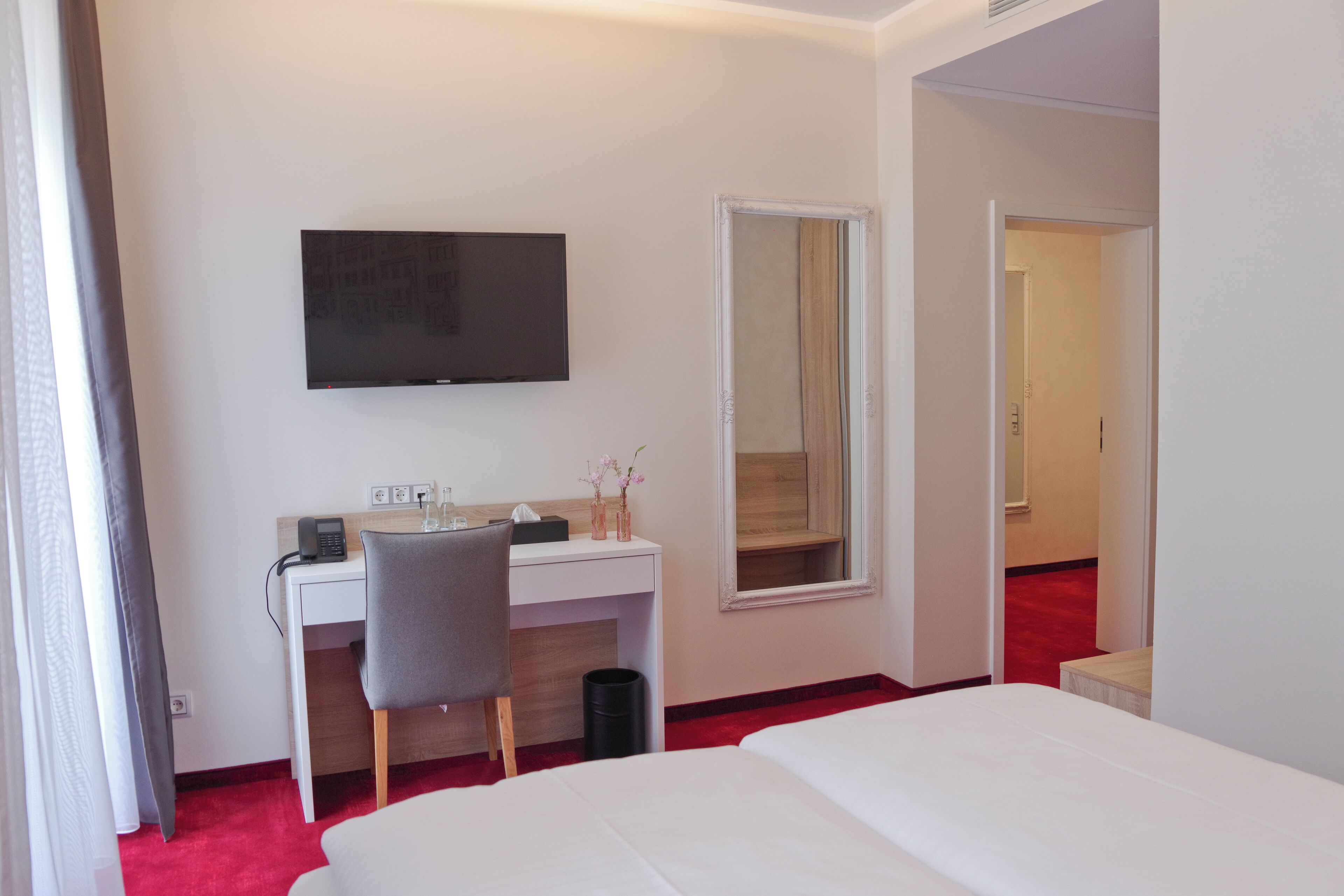 Una habitación de hotel con cama, escritorio, silla, televisión y espejo.