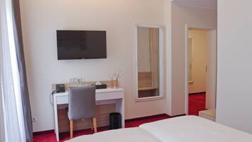 Una habitación de hotel con cama, escritorio, silla, televisión y espejo.
