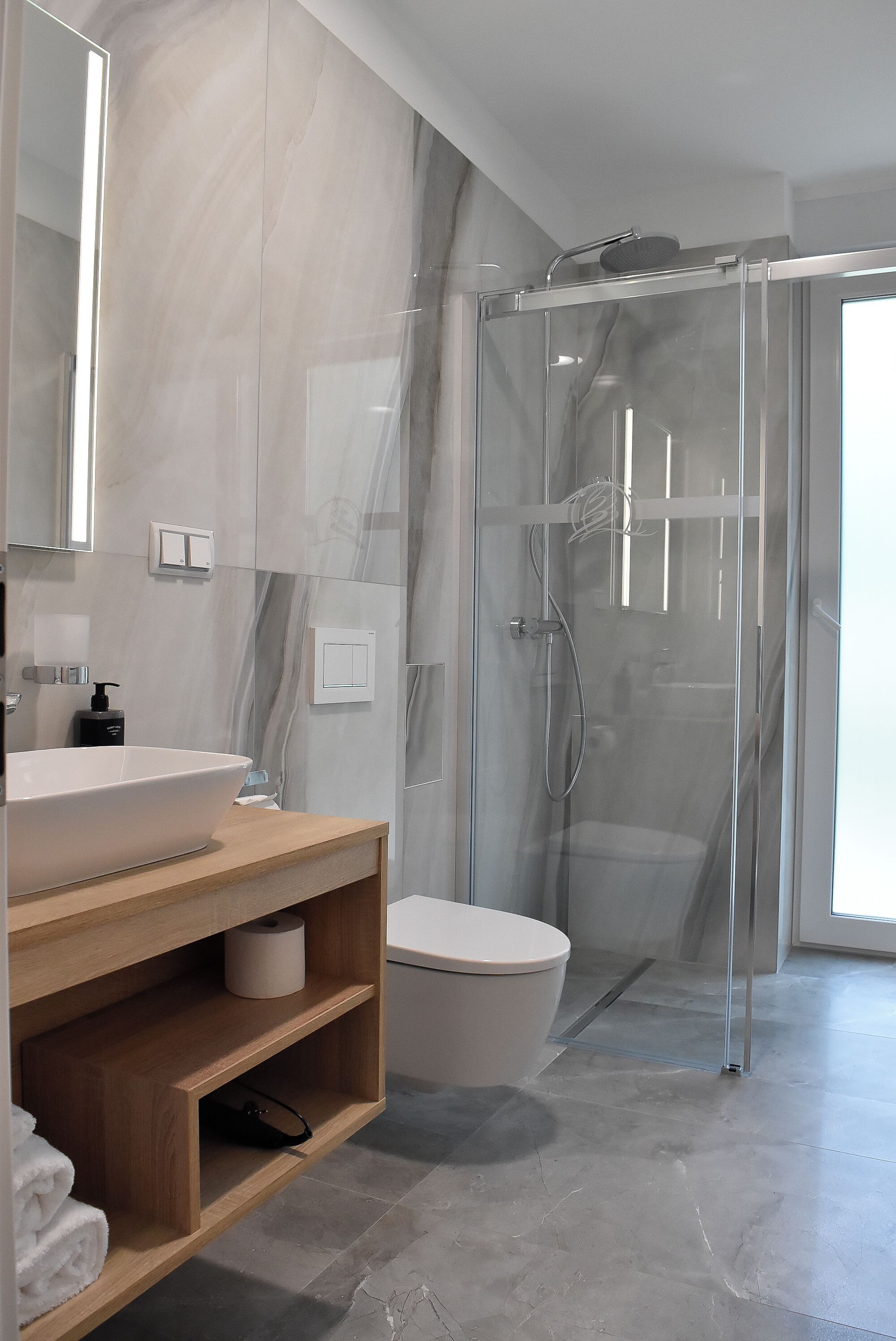 Un baño moderno con ducha envuelta en vidrio, un lavabo blanco y un mueble de tocador de madera.