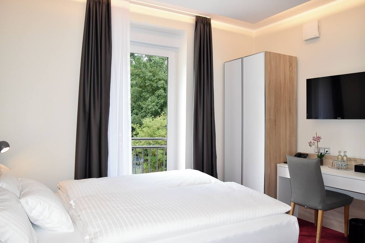 Een hotelkamer met een bed, een bureau, een stoel, een televisie en een raam met gordijnen.