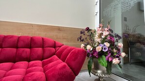Een modern interieur met een rode, beklede zithoek, een bloemstuk en een glazen deur met tekst.