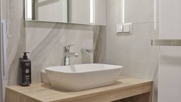Un baño moderno con un espejo grande, un lavamanos sobre encimera y un mueble de tocador de madera con estantes para toallas y artículos de aseo.