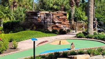 A landscaped area with a small water feature, palm trees, and a paved walkway.