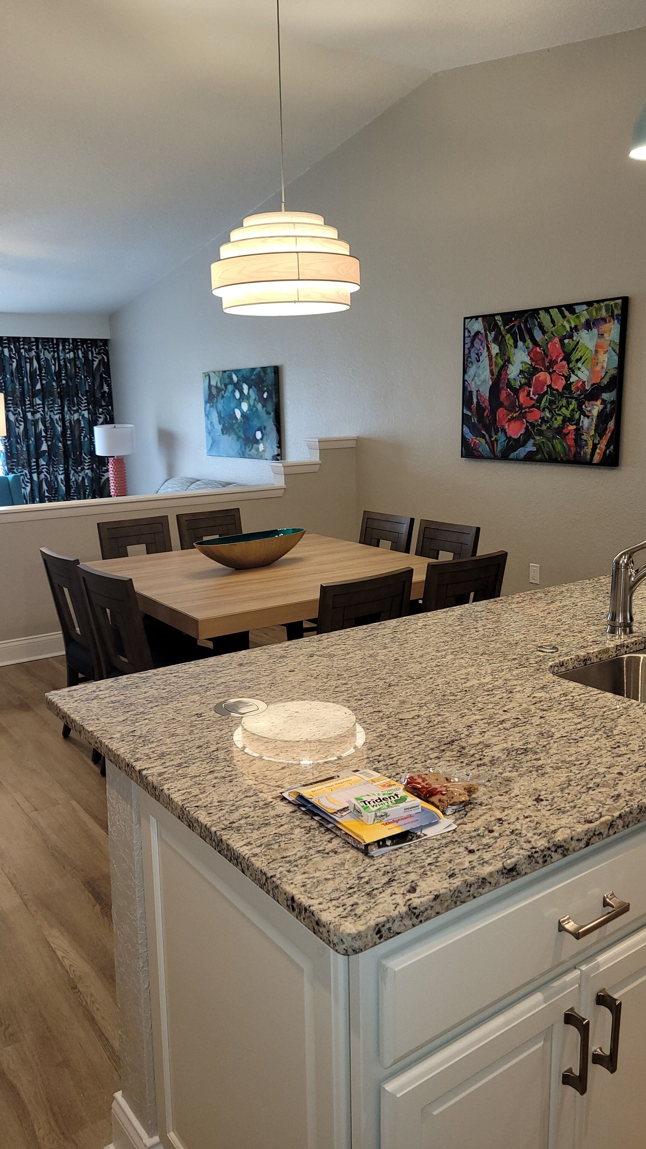 A modern kitchen with a granite countertop, a wooden dining table, and a hanging light fixture.