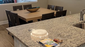 A modern kitchen with a granite countertop, a wooden dining table, and a hanging light fixture.