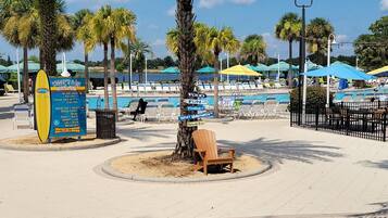 A beachside area with palm trees, a pool, lounge chairs, and a signboard.
