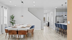 Une cuisine moderne avec des meubles blancs, un réfrigérateur en acier inoxydable et un coin bar doté de tabourets bleus.
