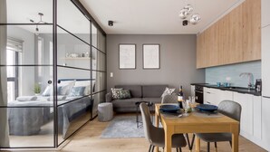 Un espace de vie moderne avec une cloison en verre séparant une chambre à coucher d’un coin repas.