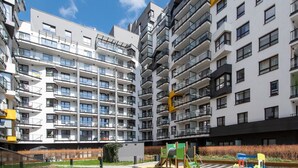 Un immeuble d’appartements moderne doté de nombreux balcons, d’une aire de jeux avec des équipements verts et d’un ciel dégagé.