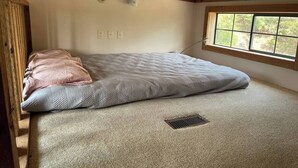A single bed with a quilt and pillows, a window with a view of trees, a wooden ceiling, and a carpeted floor. - Quiet cabin on the Brazos
 (Graham)