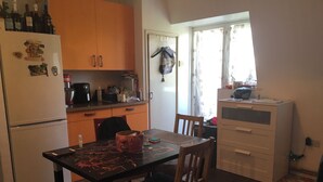 A kitchen with wooden cabinets, a refrigerator, a dining table with chairs, and a window with curtains. - Beautiful 2-bed Apartment in Dagenham (Dagenham)