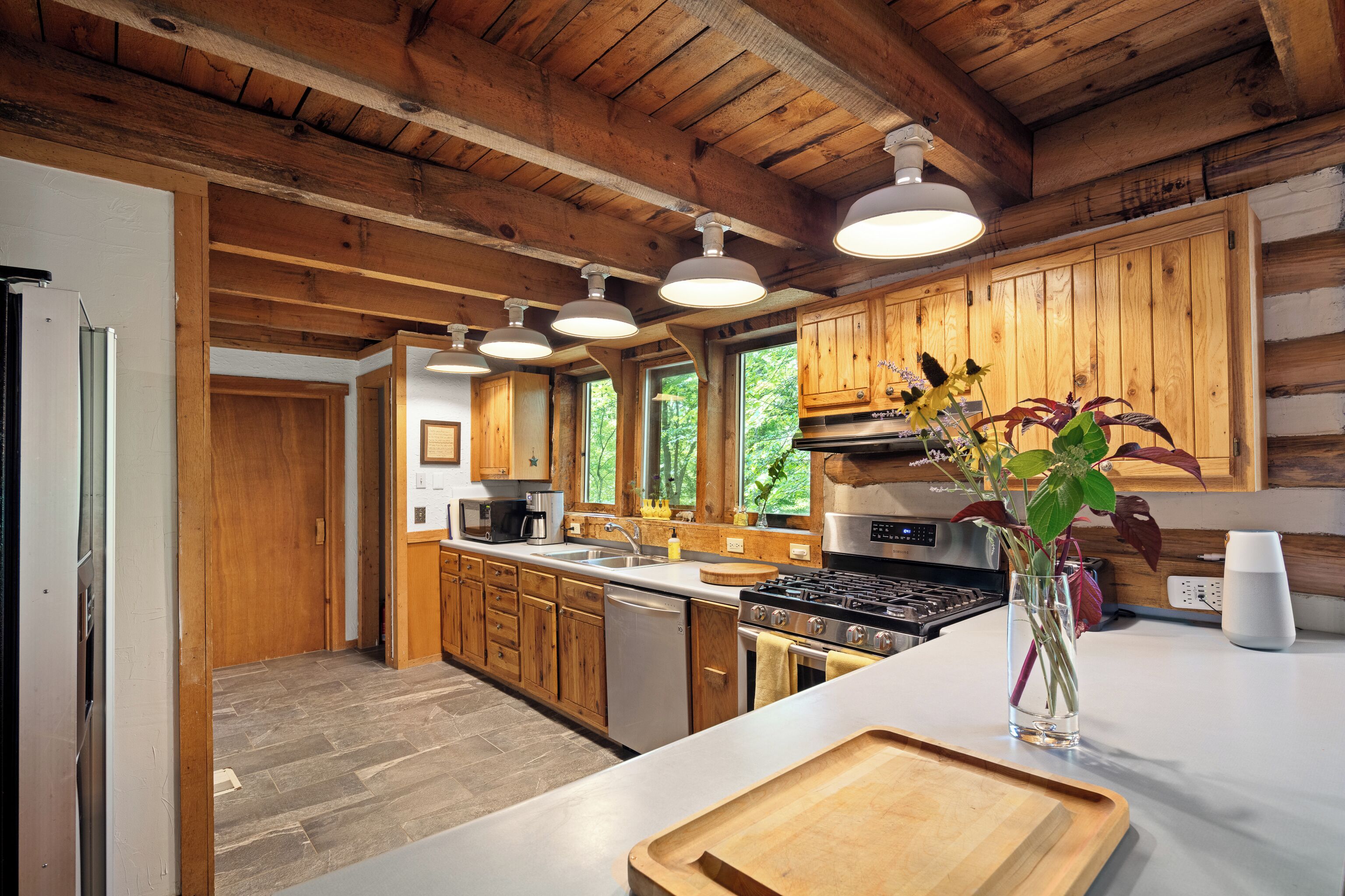 A modern kitchen with wooden cabinets, a stainless steel refrigerator, a dishwasher, a stove, and a large window providing natural light.