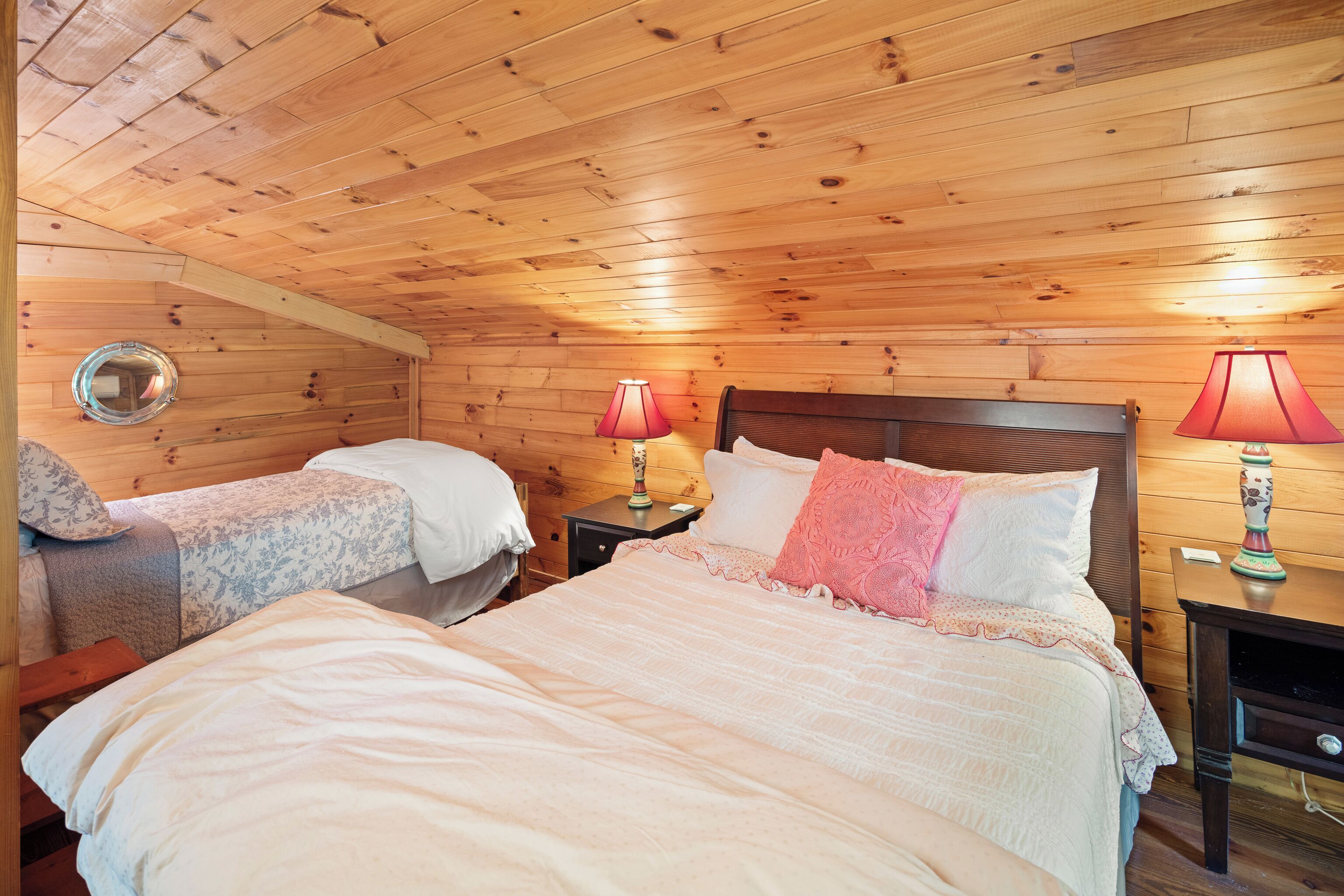 Une chambre confortable avec deux lits, des murs en bois, un miroir rond et deux lampes de chevet.