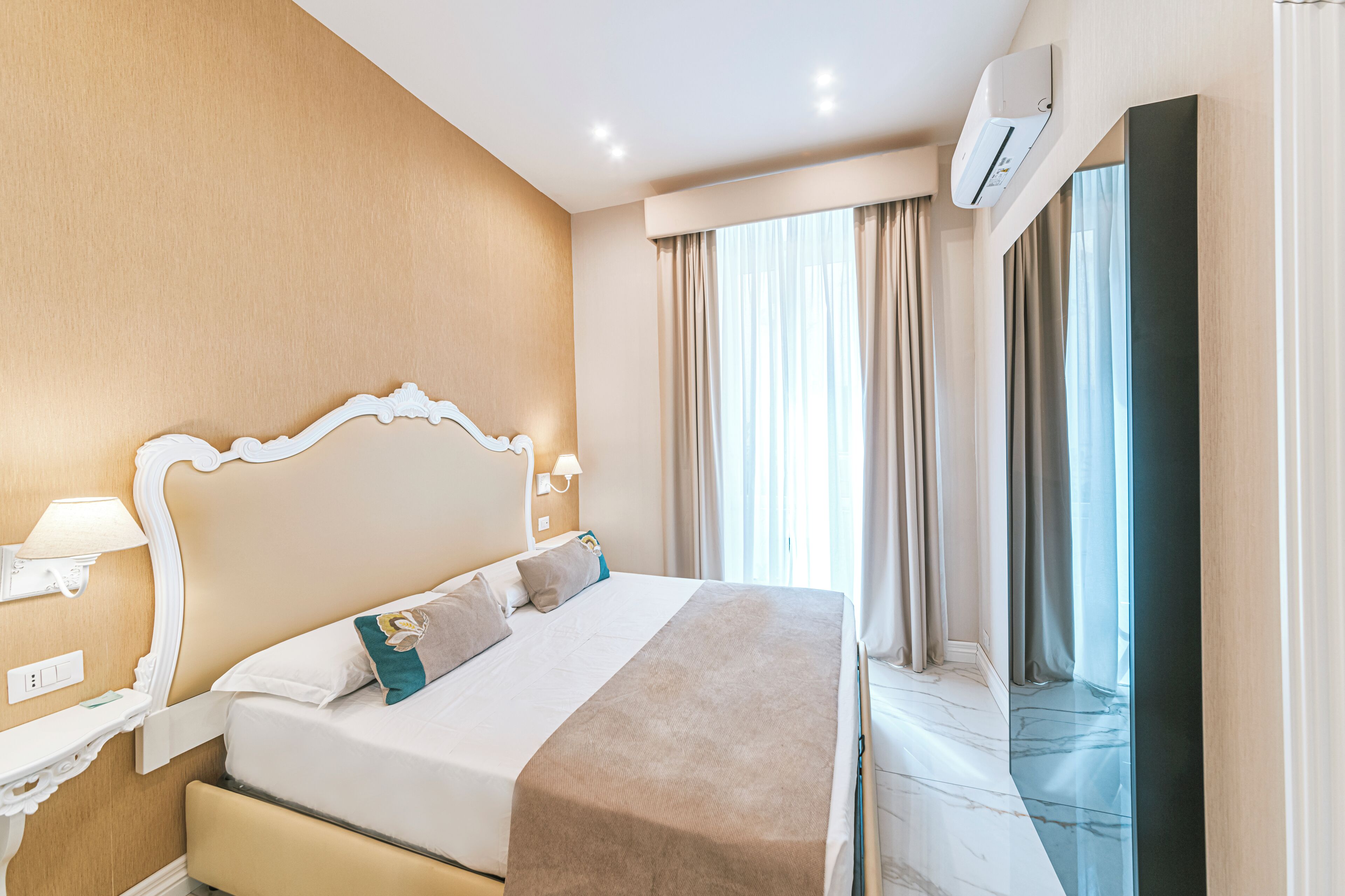 Camera d'albergo con un letto grande, un comodino, un condizionatore d'aria a muro e una finestra con tende.