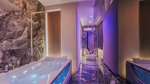 A modern spa area with marble walls, a central water feature, and a seating area with a massage chair. - GENTILE SUITE & SPA VOMERO (Naples)