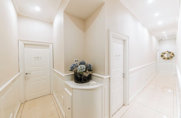 A hallway with white walls, a white door, and a small table with a floral arrangement.