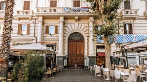 An outdoor cafe area with tables and chairs, a cobblestone path leading to a building with a large wooden door and arched windows. - GENTILE SUITE & SPA VOMERO (Naples)