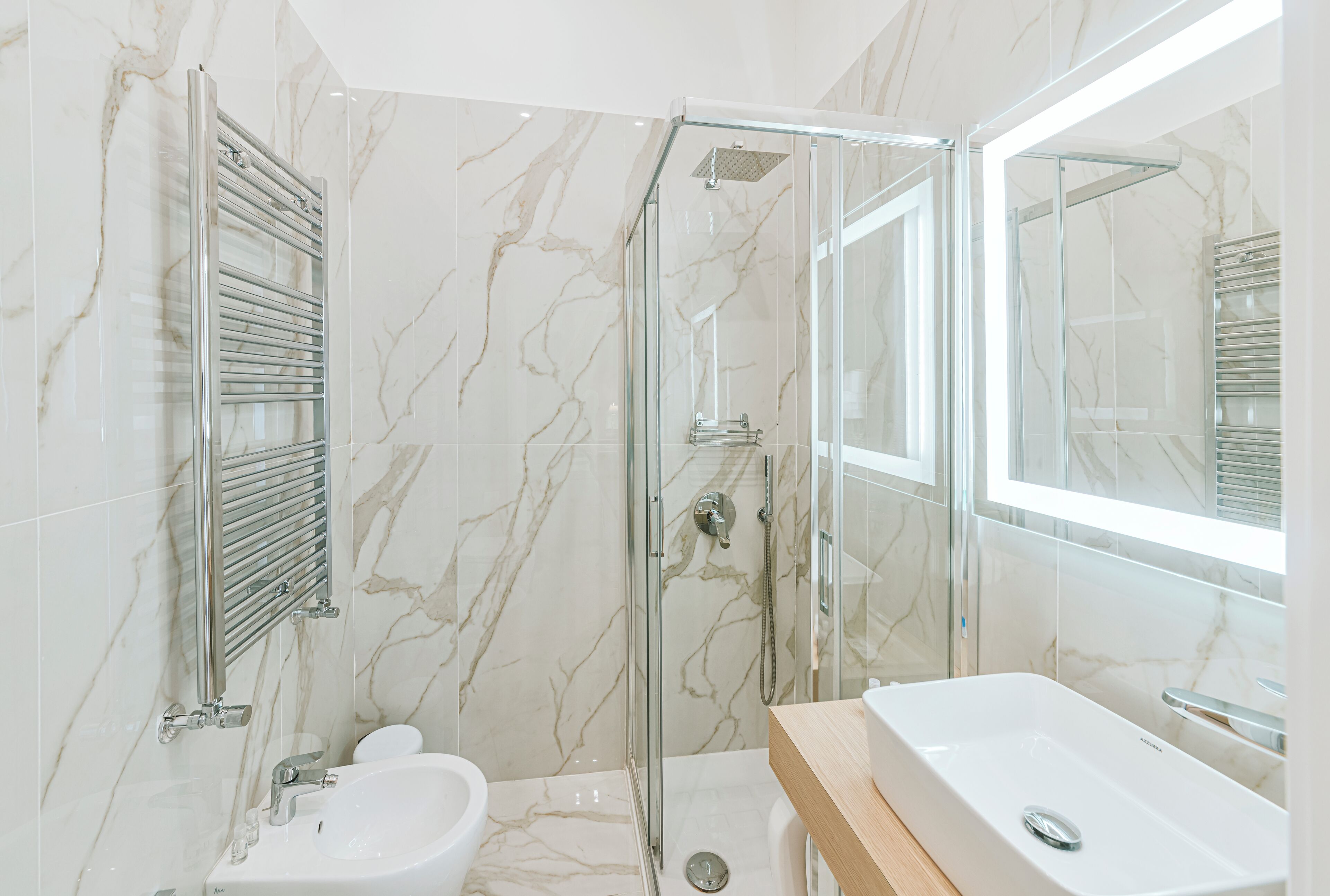 A modern bathroom with a glass-enclosed shower, a white sink, and a marble-tiled wall.