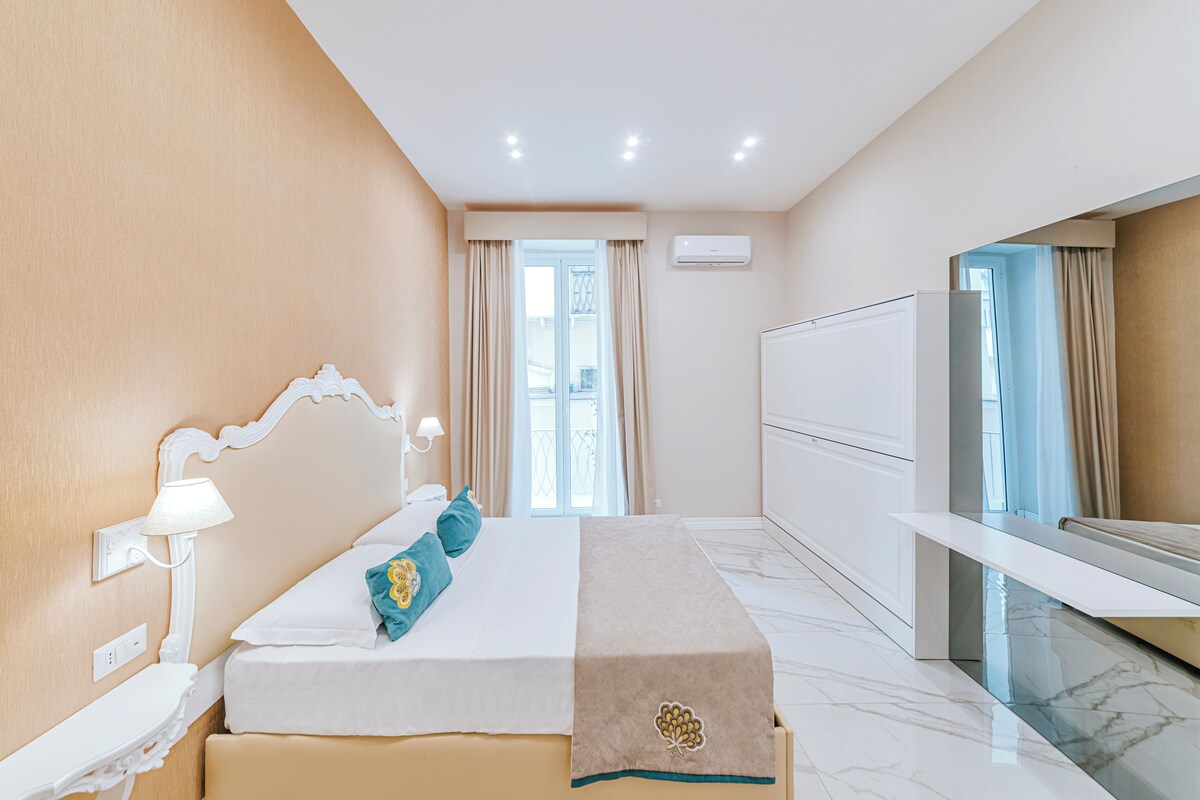 A hotel room with a bed, bedside table, lamp, and a large mirror.
