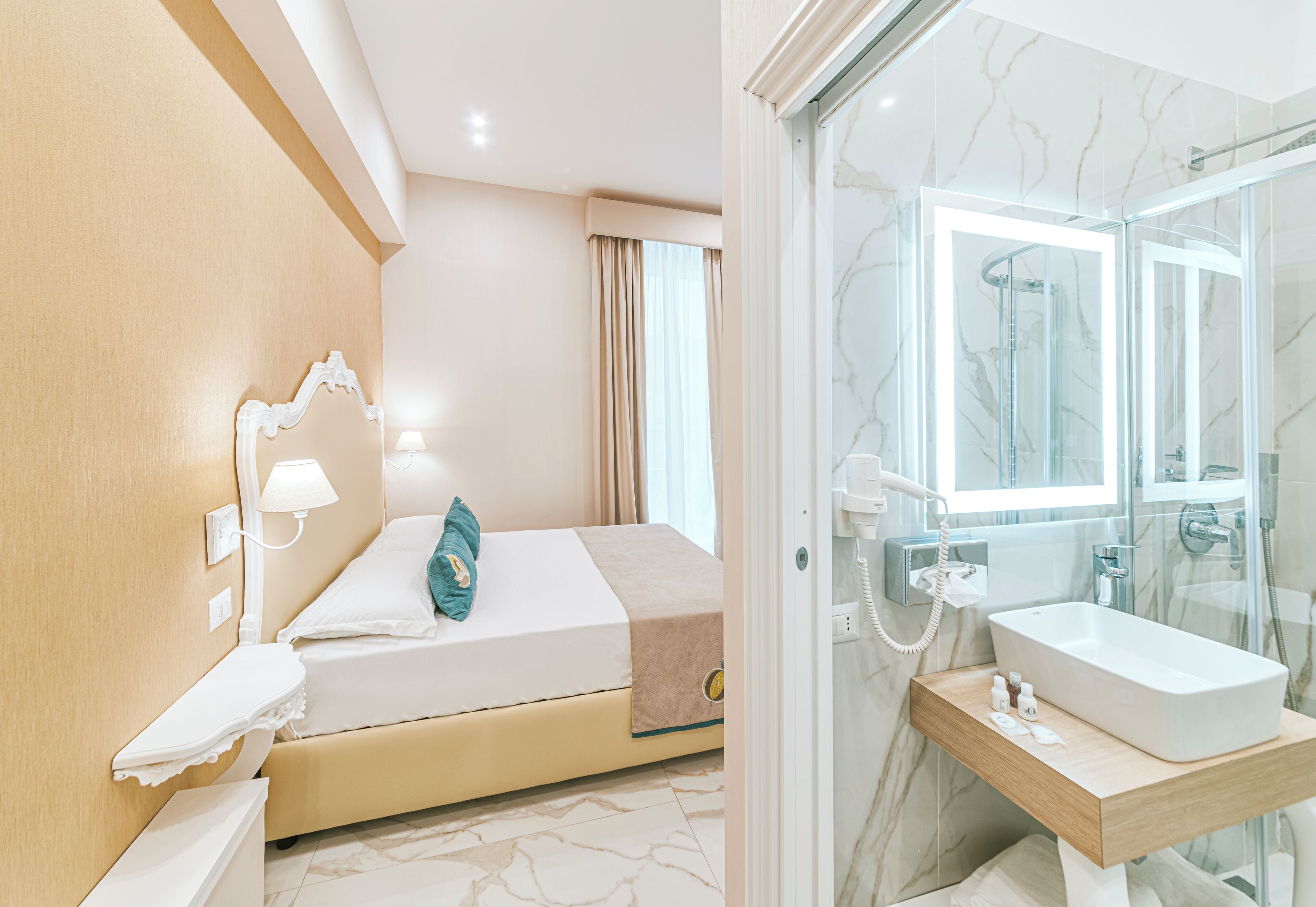 A hotel room with a bed, bedside table, lamp, and a bathroom with a sink and shower.