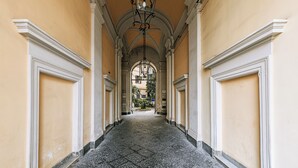 A long hallway with a tiled floor and white trim, leading to a doorway with an arched ceiling and hanging light fixtures. - GENTILE SUITE & SPA VOMERO (Naples)
