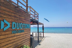 A wooden building with 'DUOTONE PRO CENTER' signage, a wooden deck, and a beach view. - Freeman Greenlees Classical Greek (Rhodes)