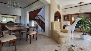 A spacious living room with a high ceiling, a dining area with wooden furniture, a stone fireplace, and a staircase leading to another level. - Freeman Greenlees Classical Greek (Rhodes)