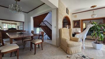 A spacious living room with a high ceiling, a dining area with wooden furniture, a stone fireplace, and a staircase leading to another level.