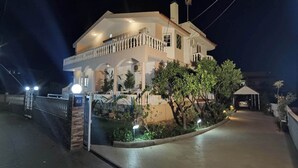 A two-story house with a balcony, a covered driveway, and a gated entrance. - Freeman Greenlees Classical Greek (Rhodes)