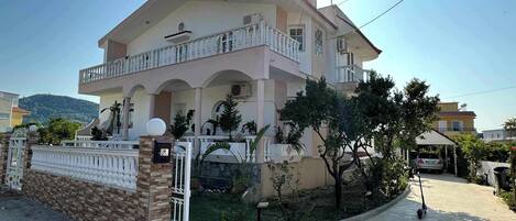 A two-story residential building with a balcony, a gated entrance, and a paved driveway.
