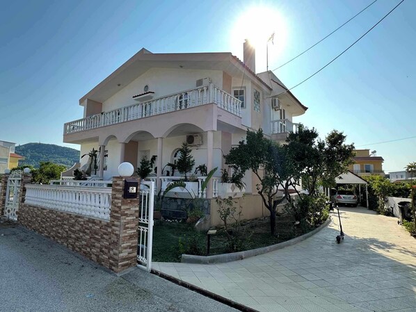Um edifício residencial de dois andares com varanda, entrada com portão e rampa de acesso pavimentada.