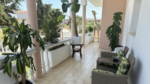 A covered outdoor area with wicker furniture, potted plants, and a white railing. - Freeman Greenlees Classical Greek (Rhodes)