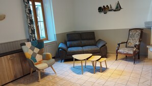 Un salon comprenant un canapé, deux fauteuils, une table basse en bois et une maquette de voilier décoratif accrochée au mur.