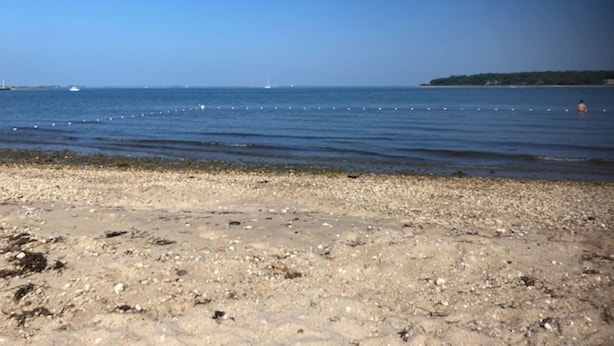 A pebbly beach with calm waters and a distant shoreline.
