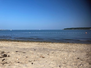 Ein kiesiger Strand mit ruhigem Wasser und einer fernen Küstenlinie.