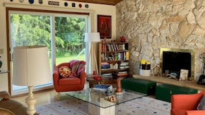 A cozy living room with a stone fireplace, a red sofa, a glass coffee table, and a bookshelf.