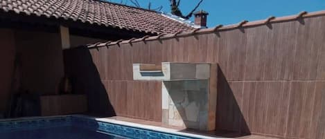 A swimming pool with a tiled pattern, surrounded by a building with a tiled roof and a stone wall.