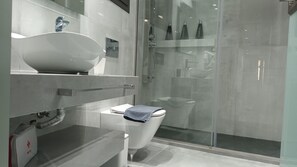 Een moderne badkamer met een groot wit wastafel, toilet, douchecabine van glas en een medicijnzak op het aanrecht.