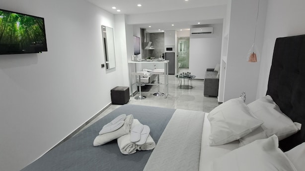 A modern hotel room with a bed, a TV, a bathroom, and a dining area. - KM LUXURY apart downtown (Heraklion)