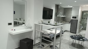 A modern, compact hotel room with a kitchenette, a bed with a white headboard, a small seating area, and a glass table with drinks. - KM LUXURY apart downtown (Heraklion)